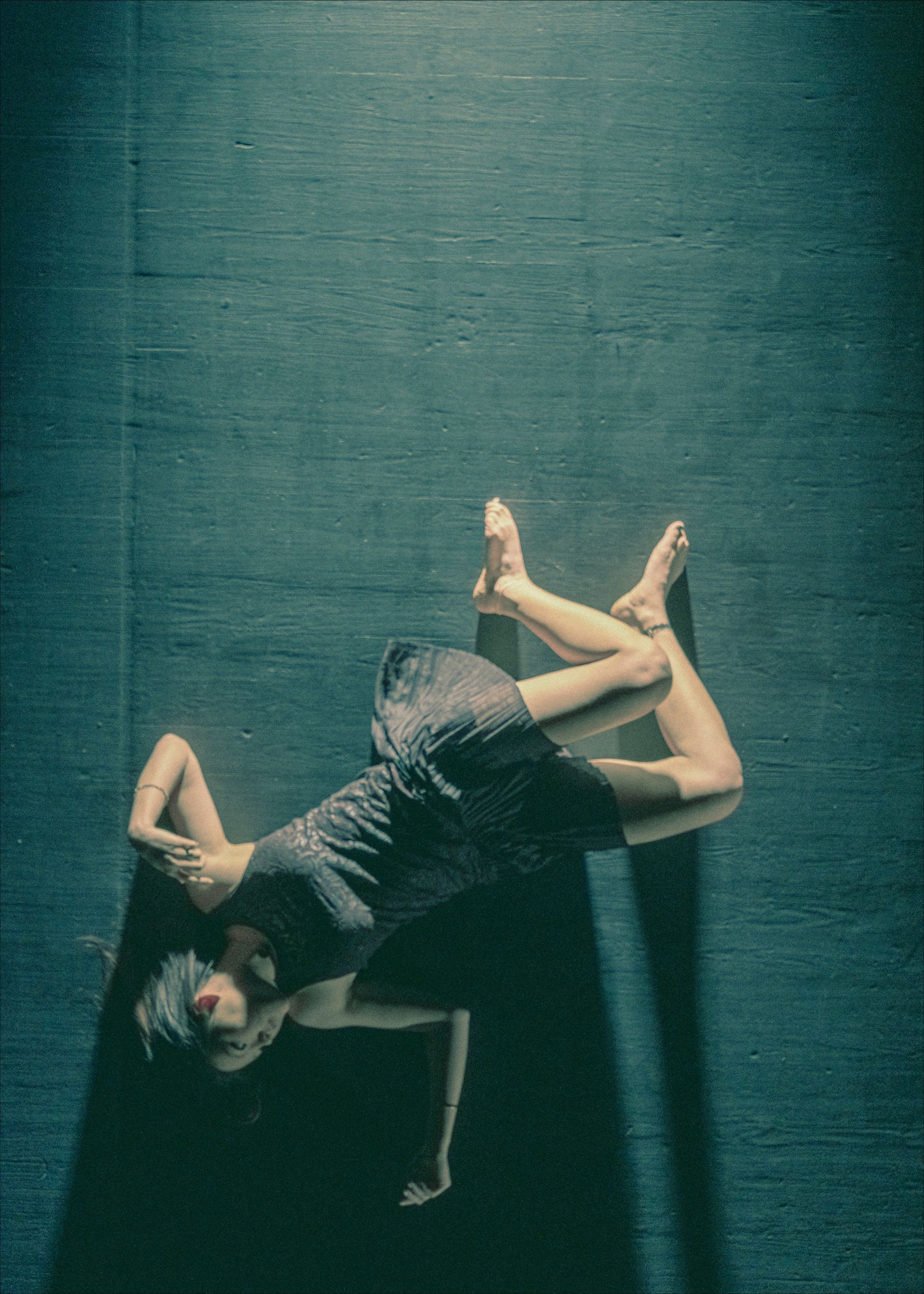 A person in a black dress lying on their back with arms above the head, legs crossed.