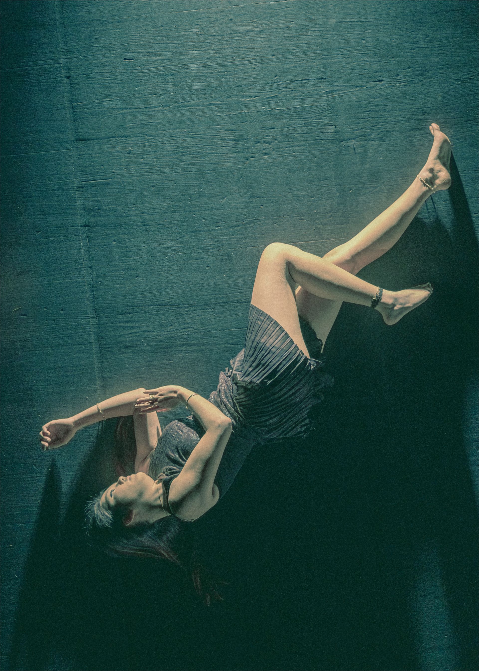 Woman in a dark dress floating on a dark surface, arms and legs outstretched.