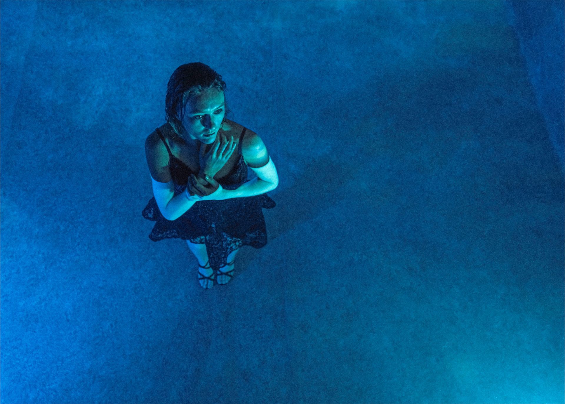 Woman in a dark dress, arms crossed over chest, in blue-lit water.