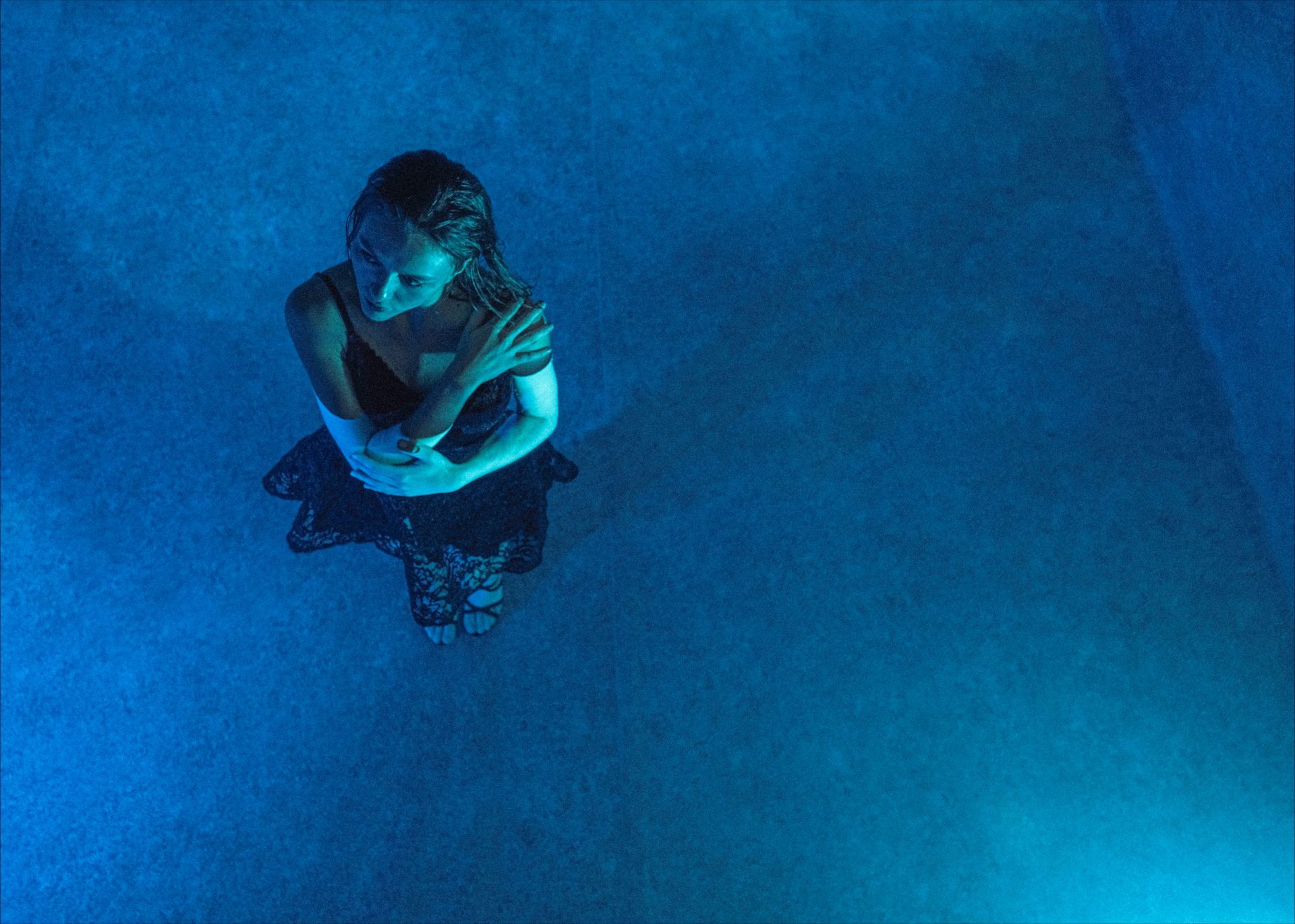 Woman in blue light, arms crossed, looking down, in a misty environment.
