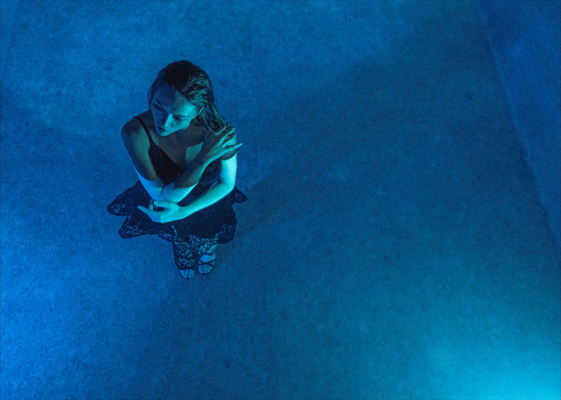 Woman in dark dress, arms crossed, lit by blue light.