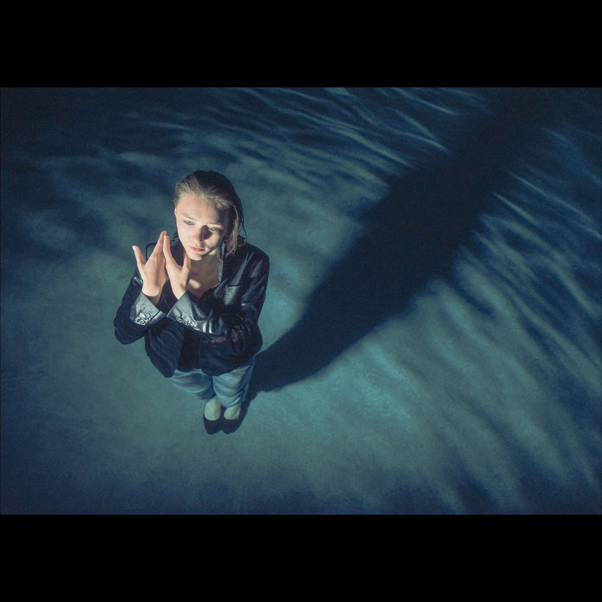 Woman clapping underwater, shadow cast on the water, blue and dark tones.