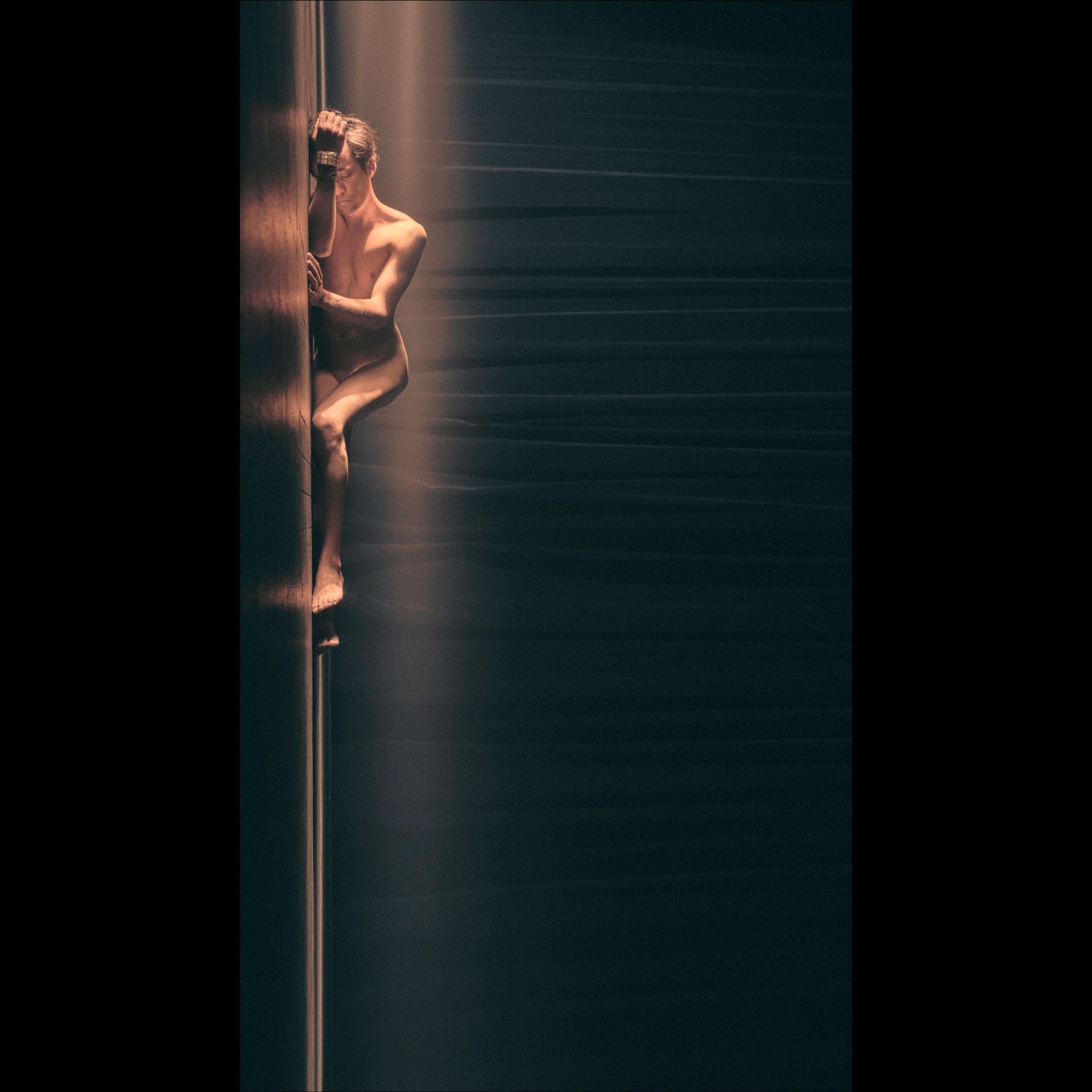 Naked person climbing a dark wall, lit from the side. Horizontal streaks blur the background.