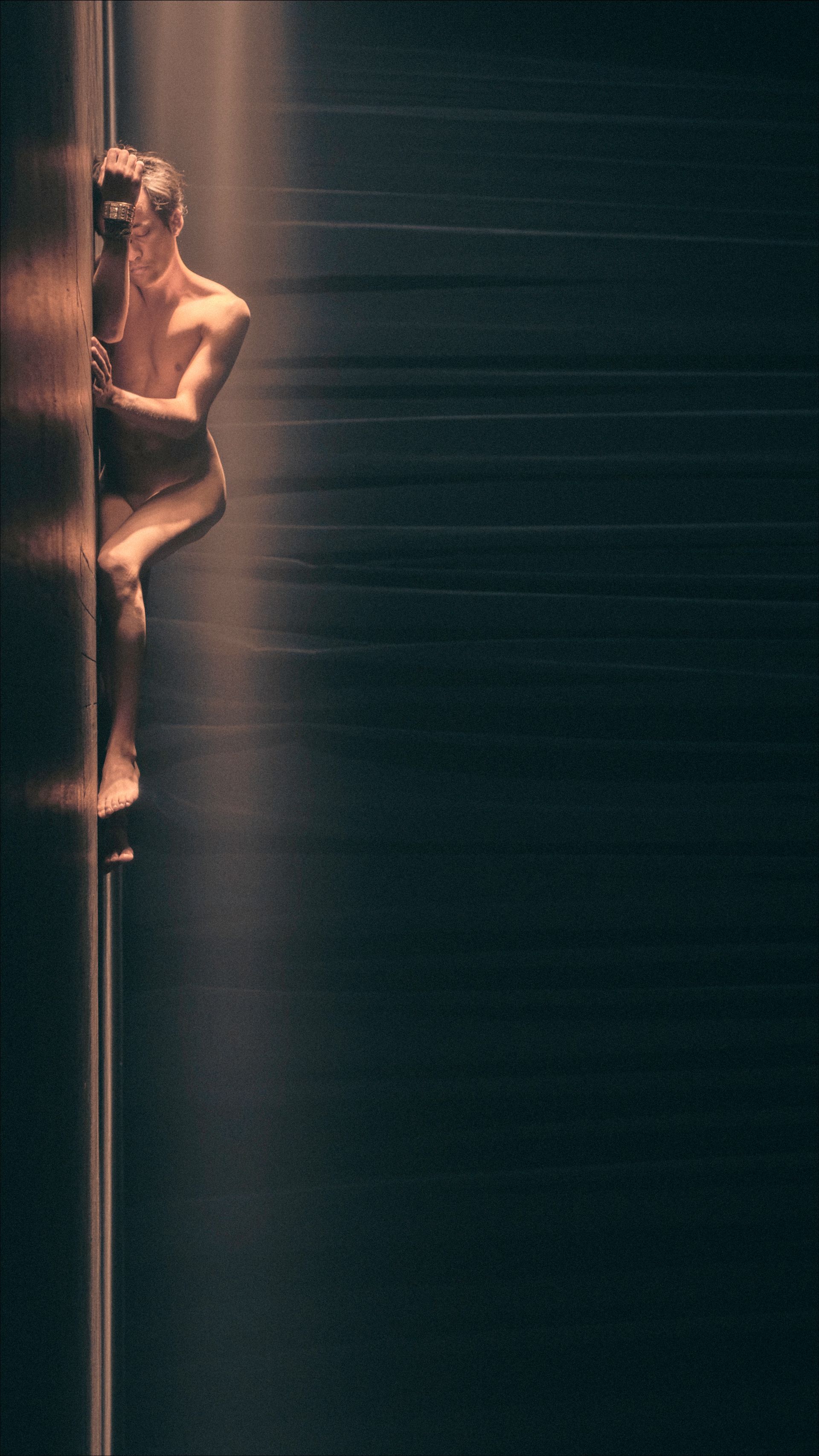 Man clinging to a dark, vertical surface; dramatic lighting.