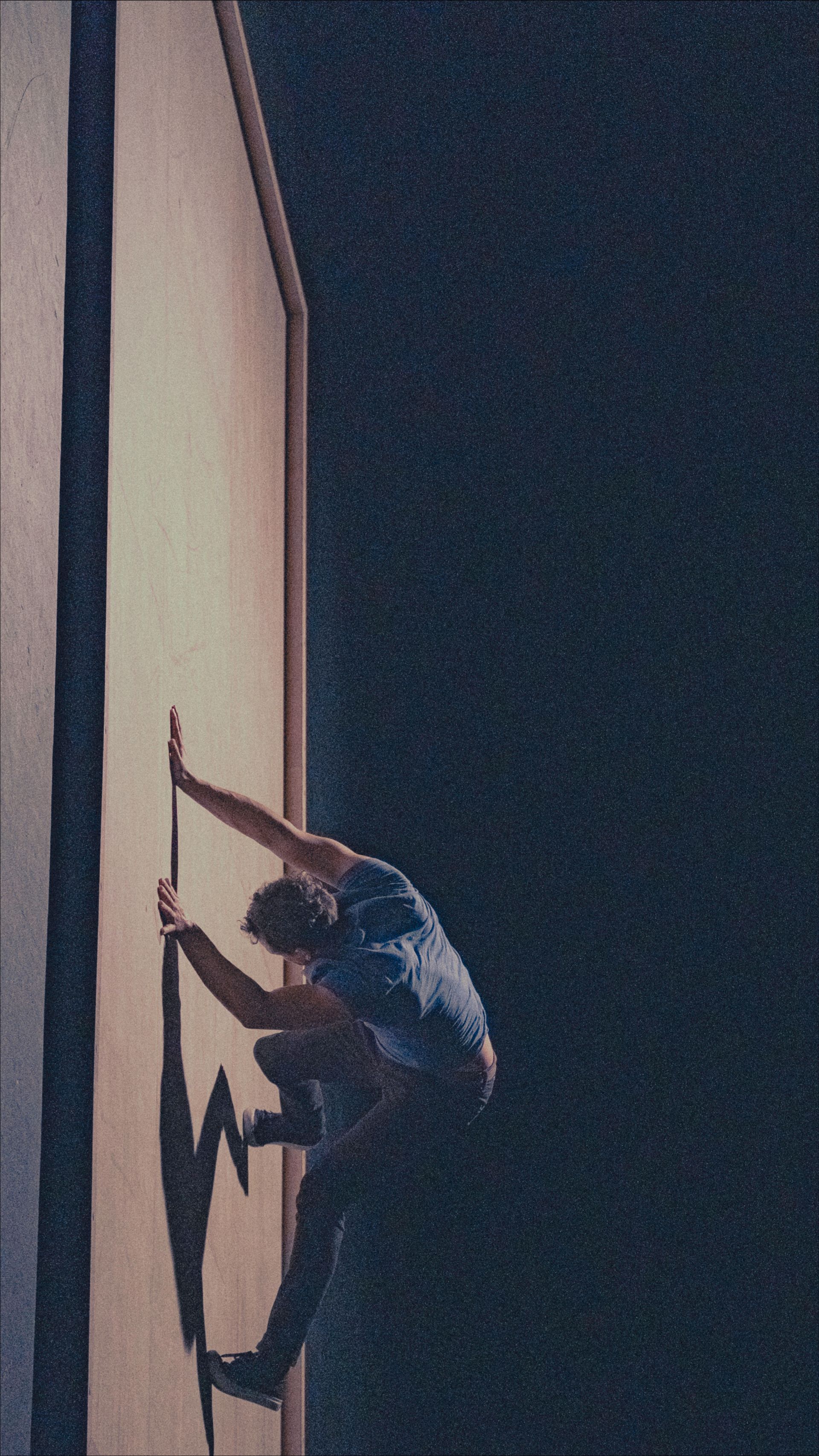 A person climbing a wall with a pole, silhouetted against a dark background.