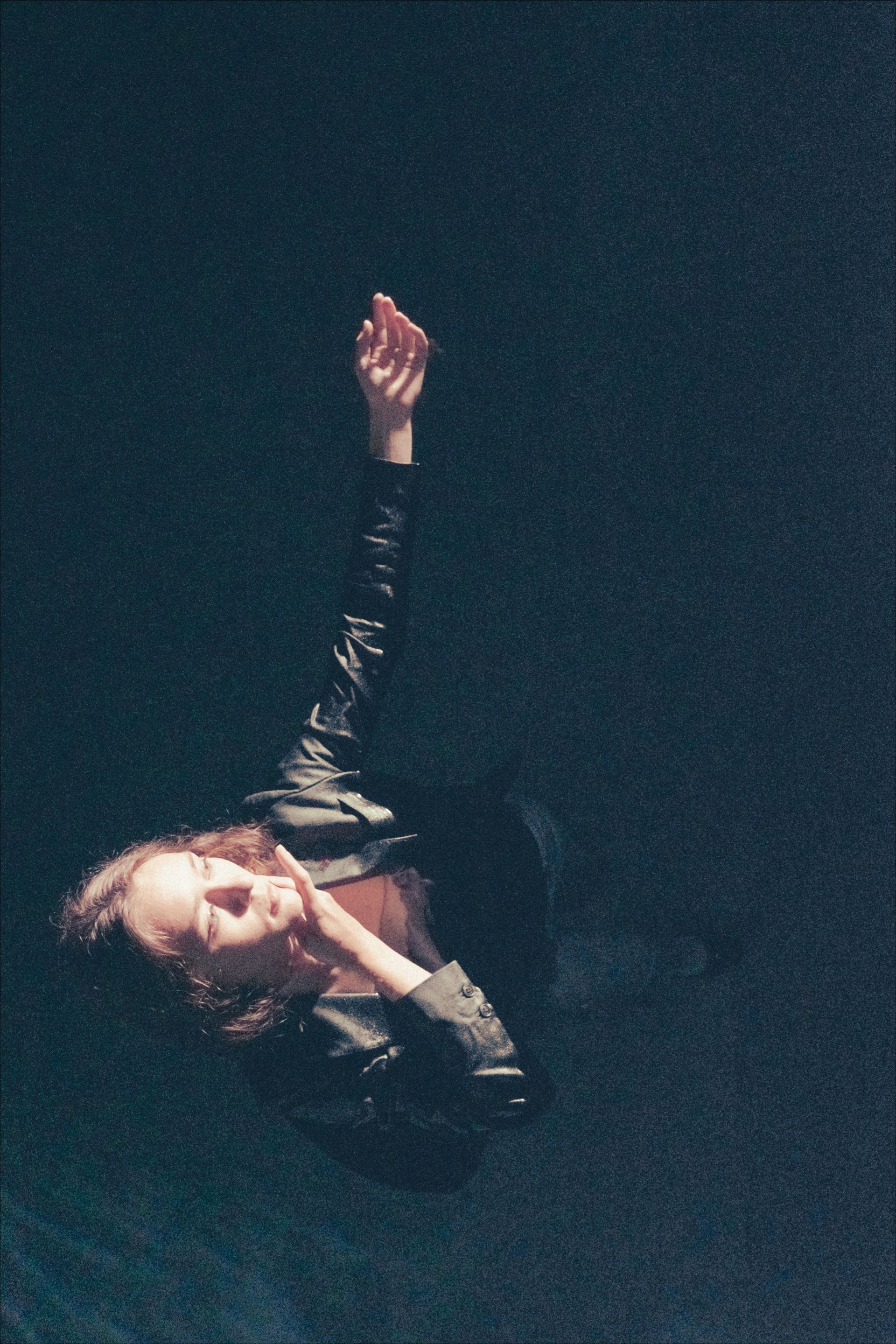 Woman reaching up with arm extended, dark setting.