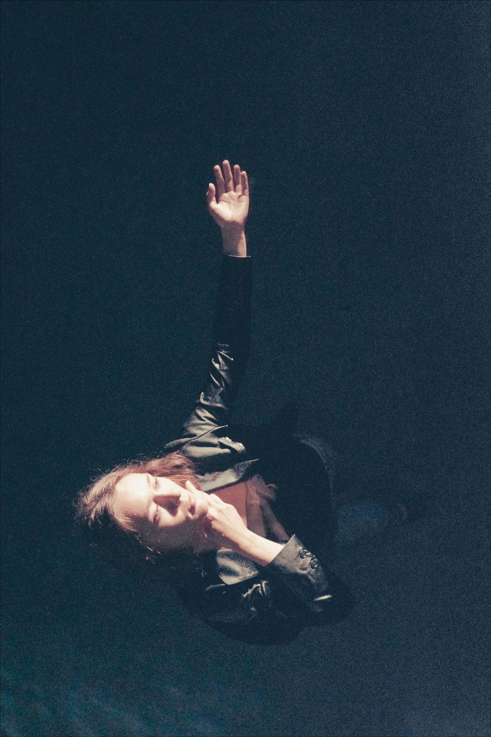 A person with an arm raised, seemingly reaching upwards, against a dark background.