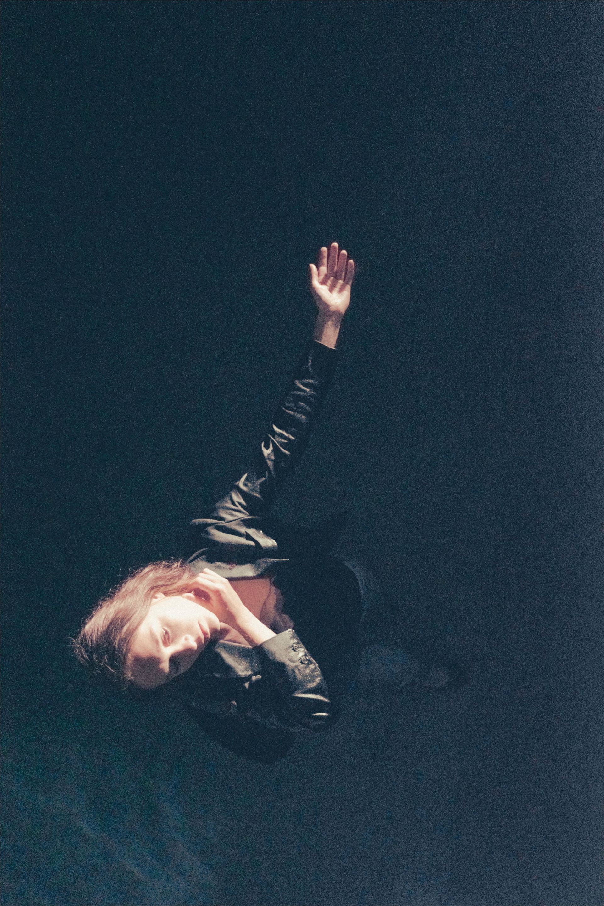 Person with arm raised reaching upward in dark, textured background.