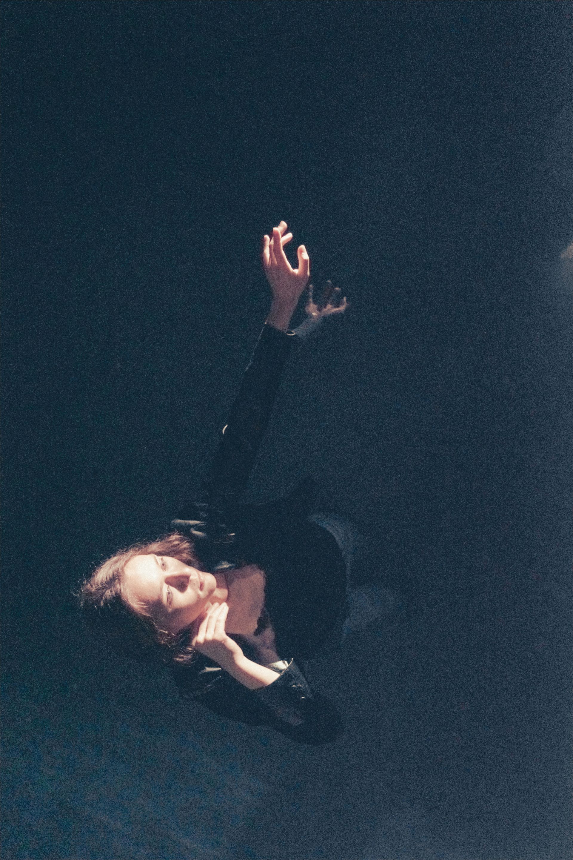 Person, dark clothing, arms raised, head tilted back, soft lighting.