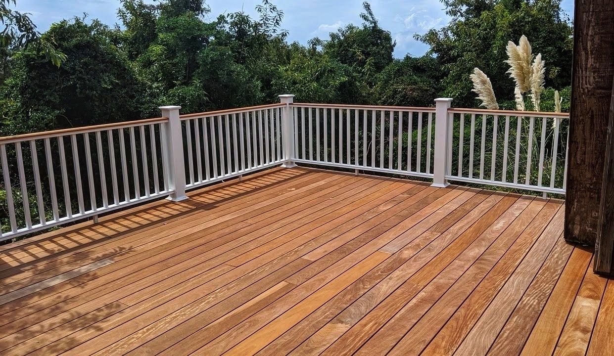 Wooden deck with white railing overlooking lush greenery.