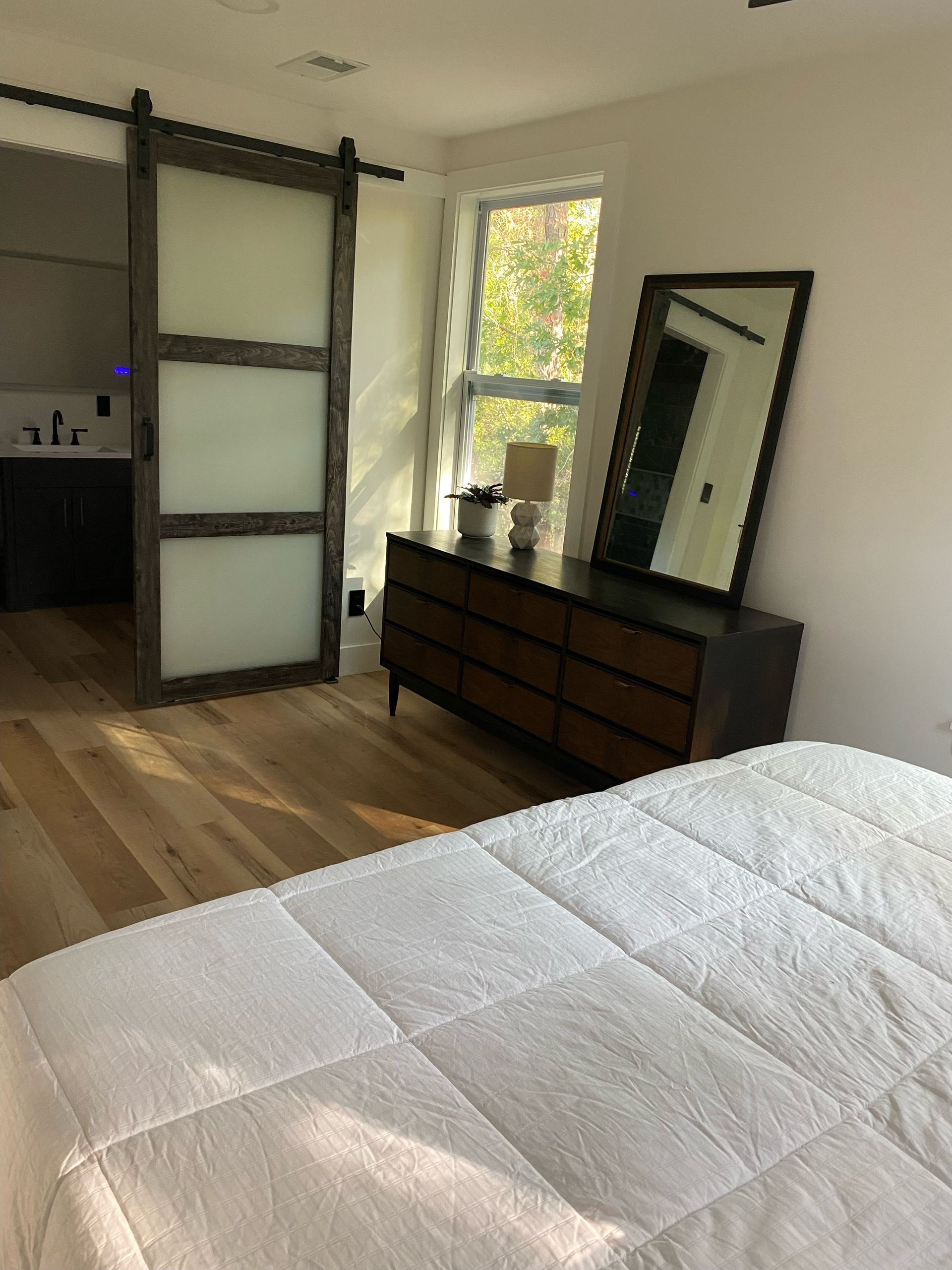 Bedroom with wooden floors, a dresser, mirror, and frosted-glass sliding barn door leading to a bathroom.