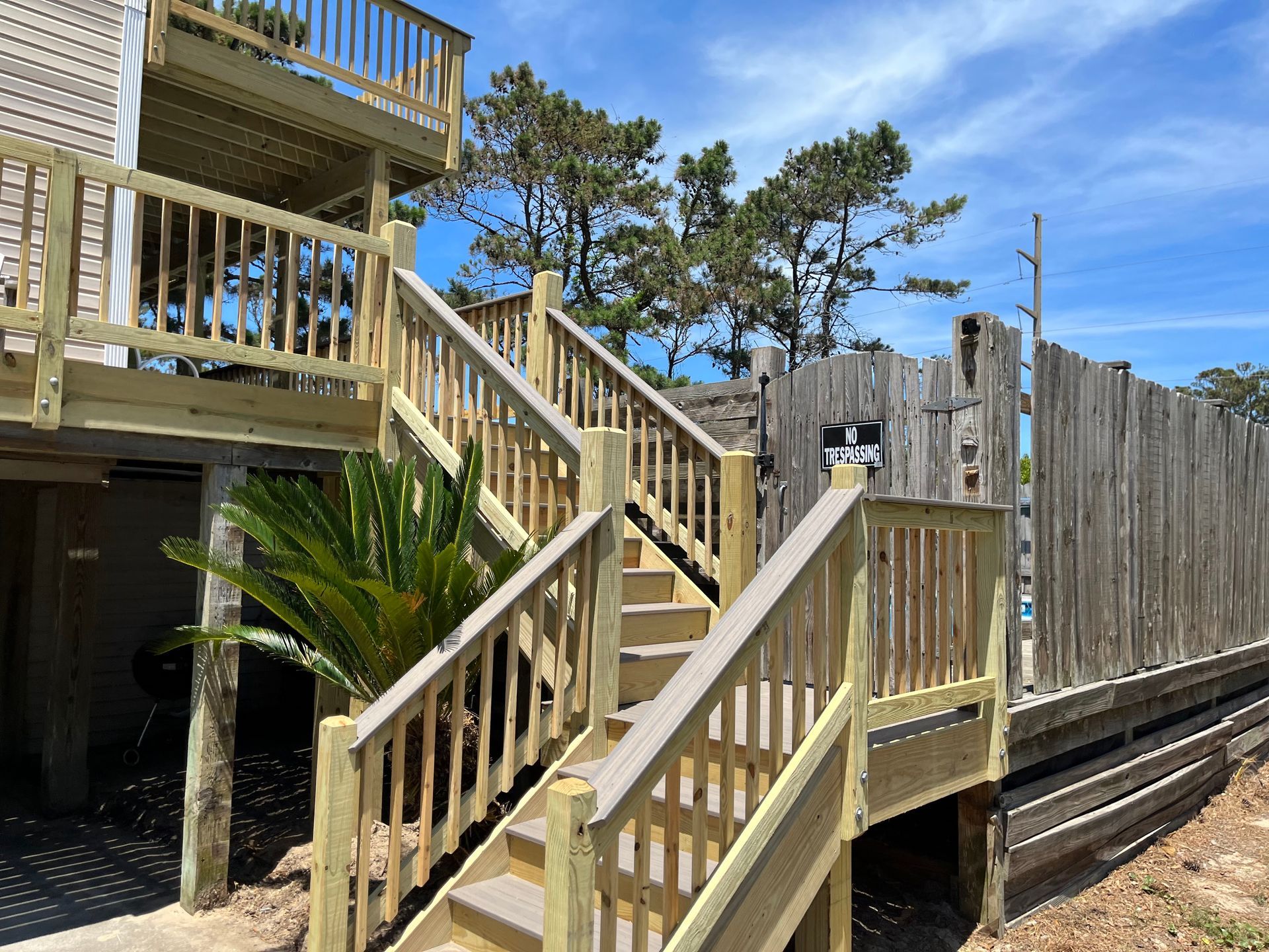 Wooden stairs leading up to a deck, next to a wooden fence, against a sunny sky.