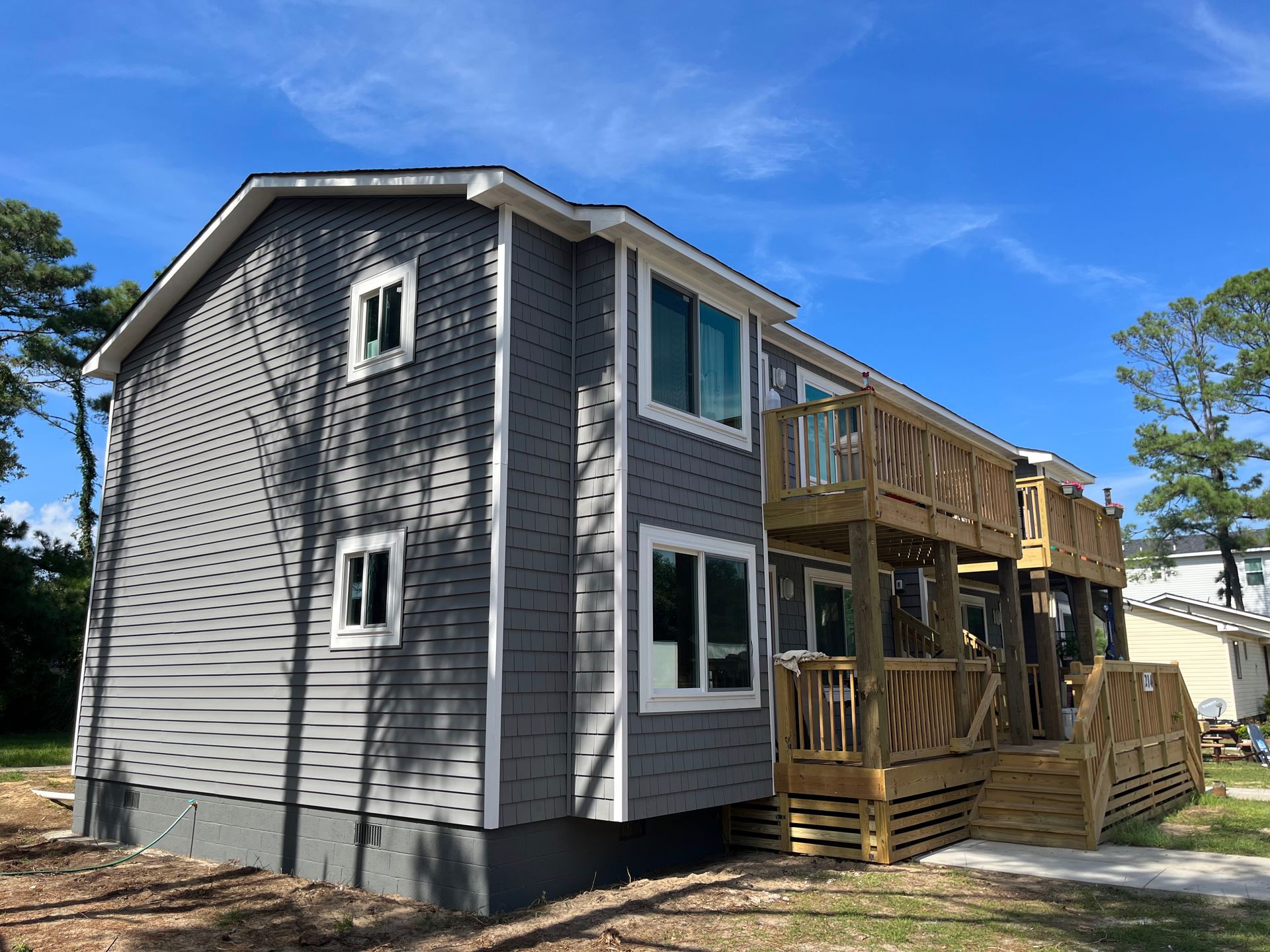 Two-story building with grey siding and a wooden deck. Blue sky background.