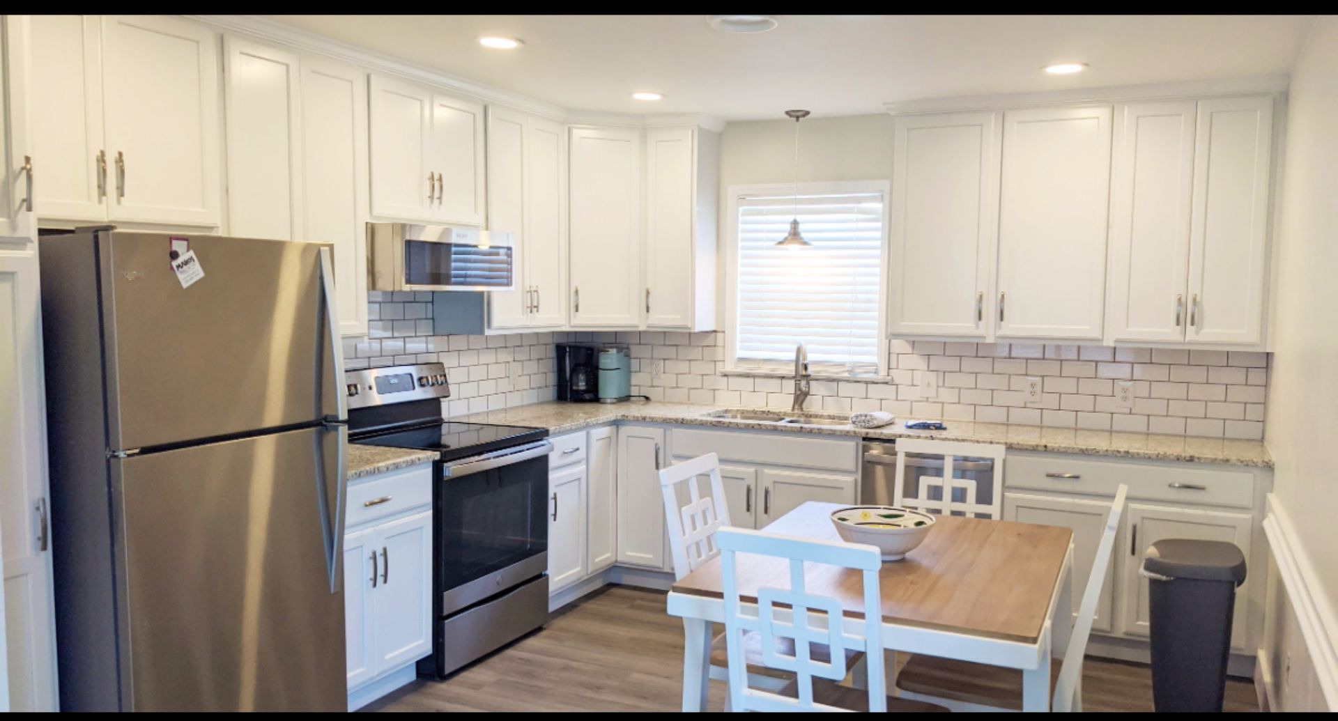 White kitchen with stainless steel appliances, granite countertops, and a small dining table.