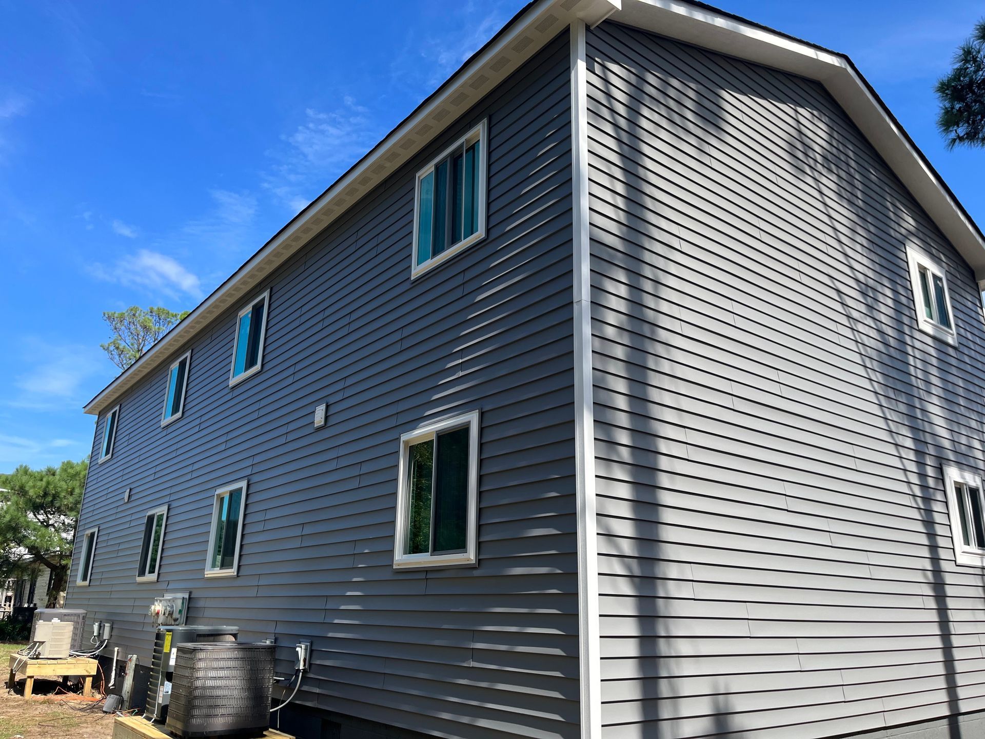 Two-story building with gray siding and white trim against a bright blue sky. Windows are present on each level.