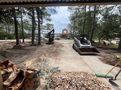 Construction site with mini excavator and skid steer on dirt path, building in the background.