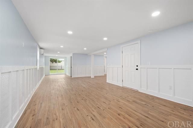 Empty room with wood-look flooring, light blue walls, white wainscoting and trim, and a white door leading to another area.