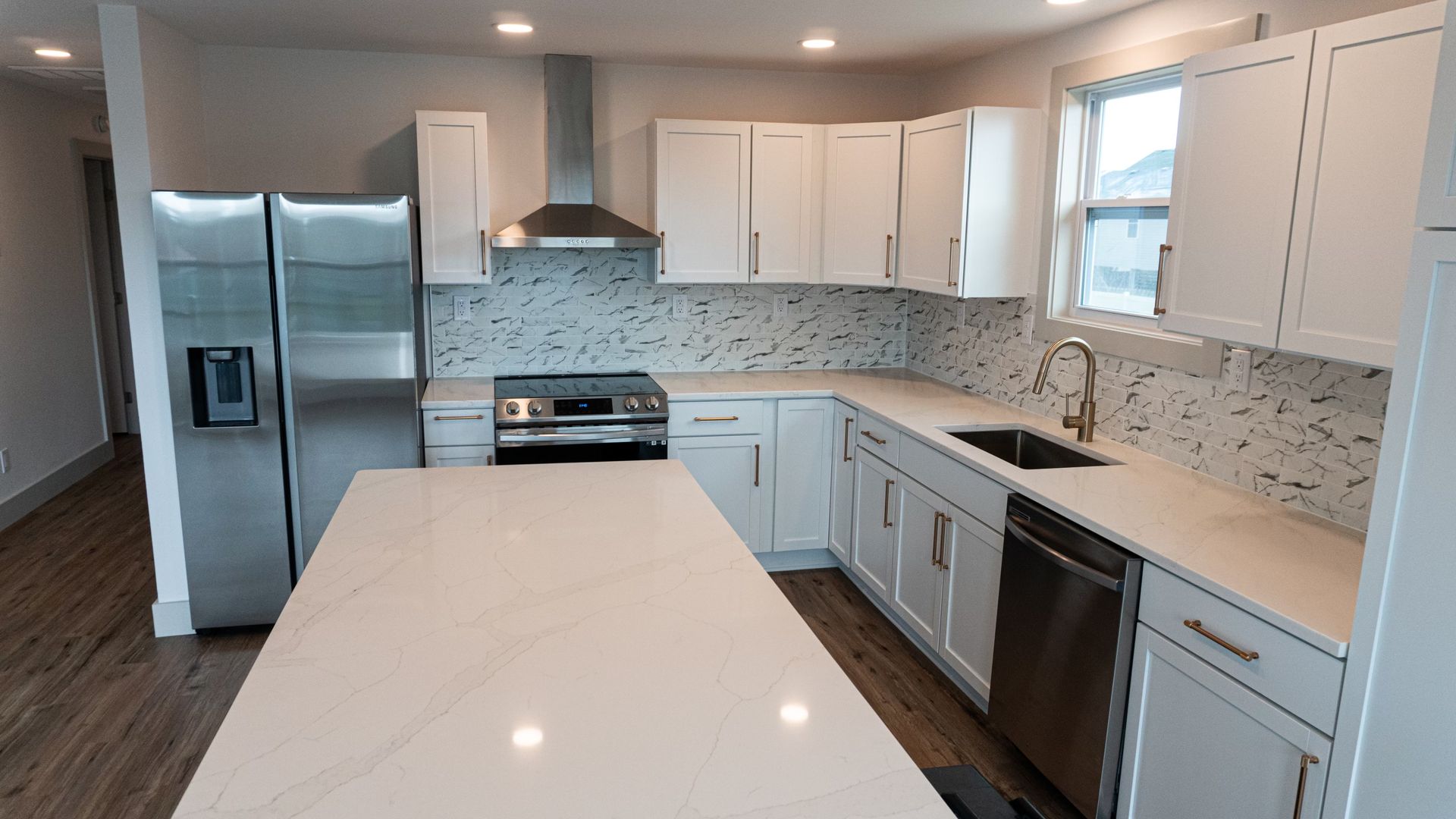 Modern white kitchen with stainless steel appliances, a large island, and patterned backsplash.