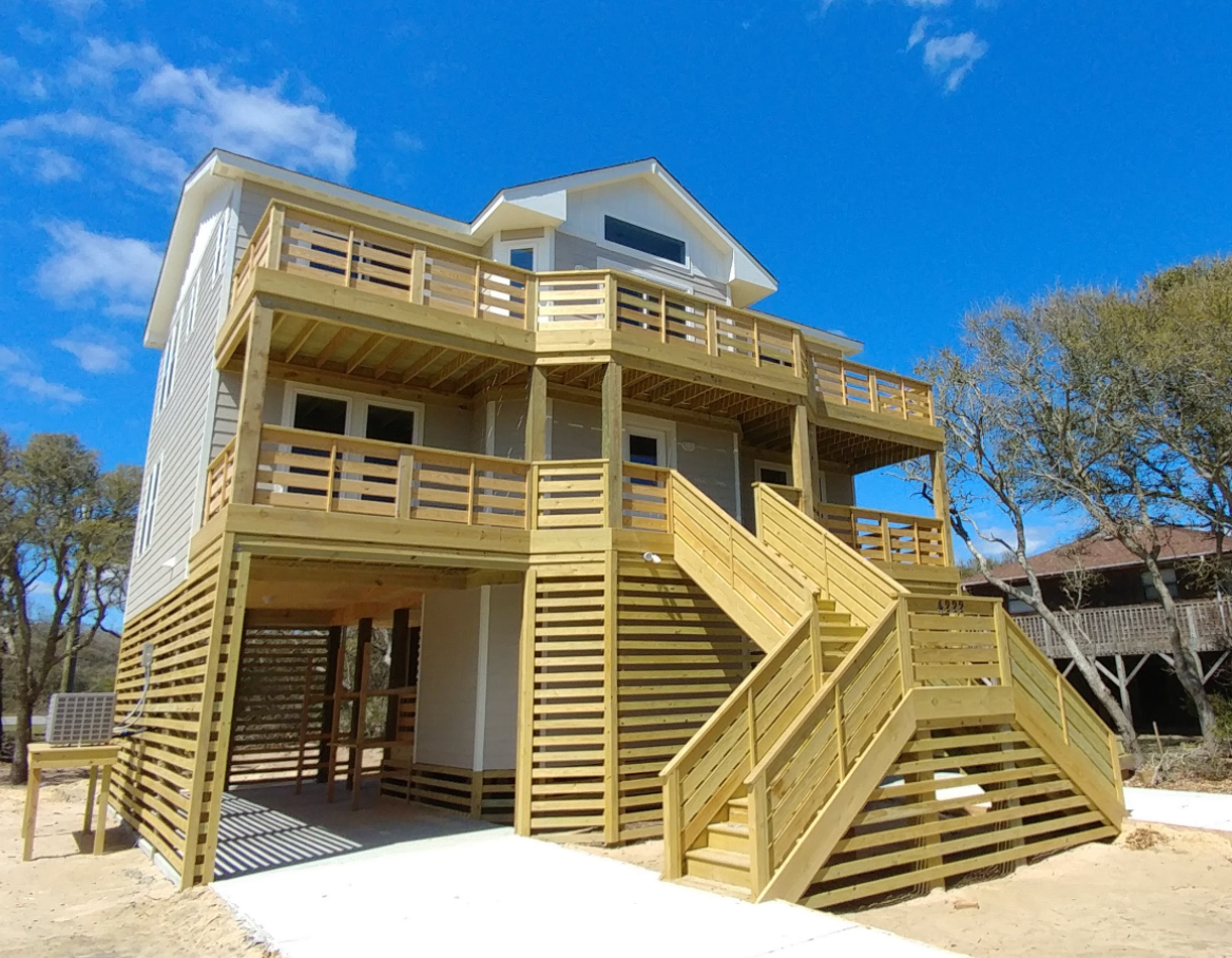Beach house on stilts with light siding, multiple decks, and a wooden staircase leading up to the entrance