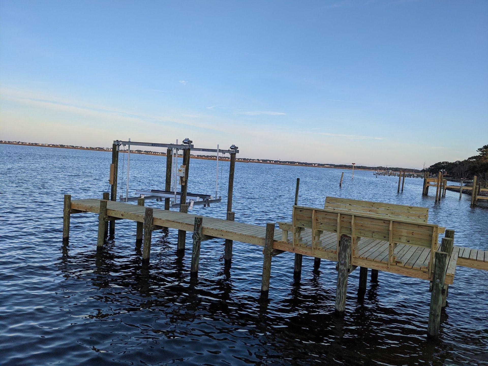 A newly built wooden pier extending into calm water, under a blue sky.