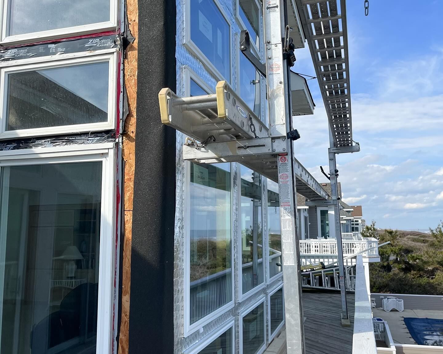 A construction site with scaffolding on a building's side, where windows are being installed. 