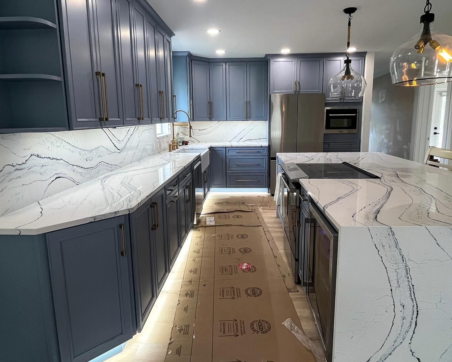 Newly renovated kitchen with blue cabinets, white countertops with dark veining, and a large island.