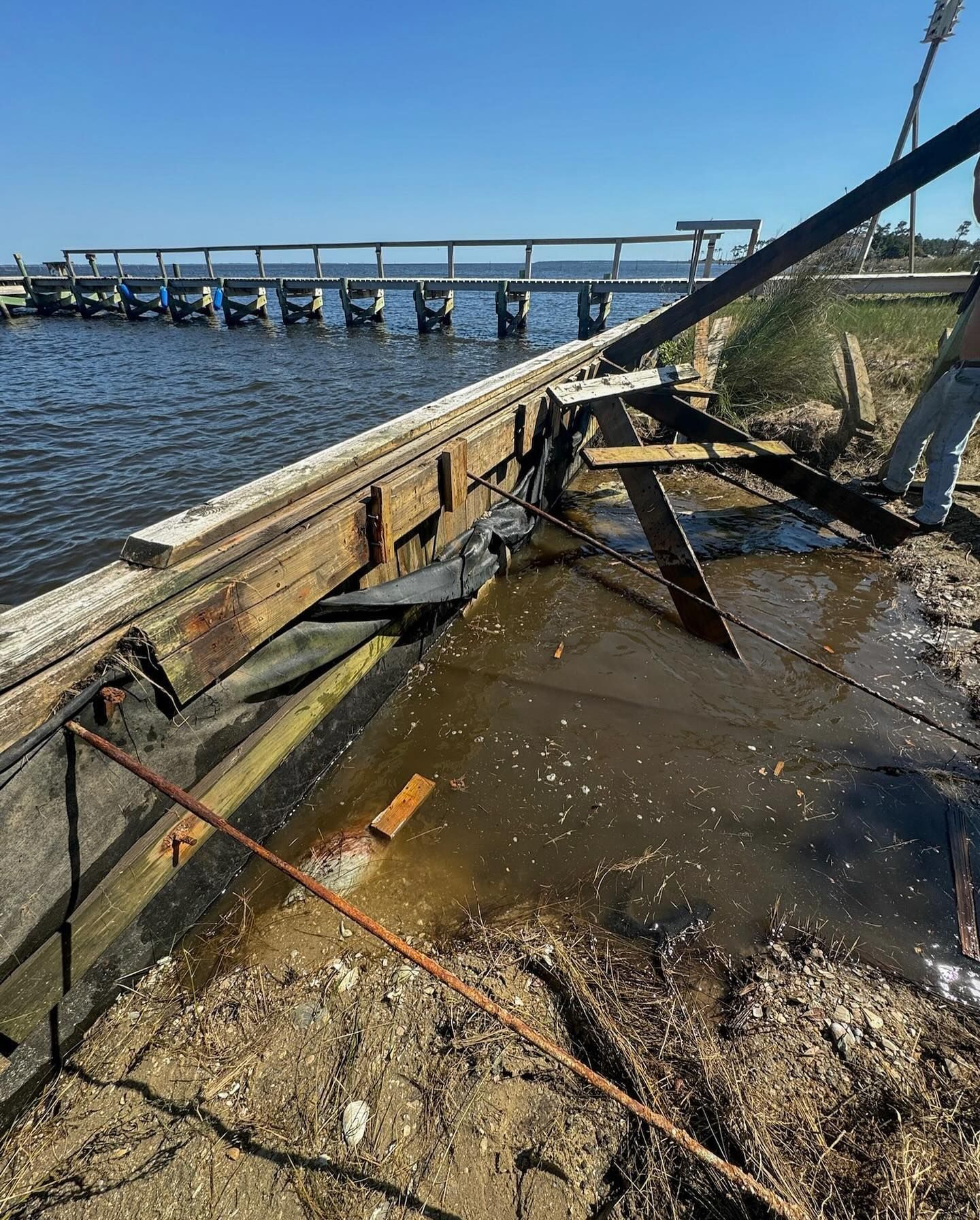 Damaged wooden dock with a section collapsing into water, with a person in the background.