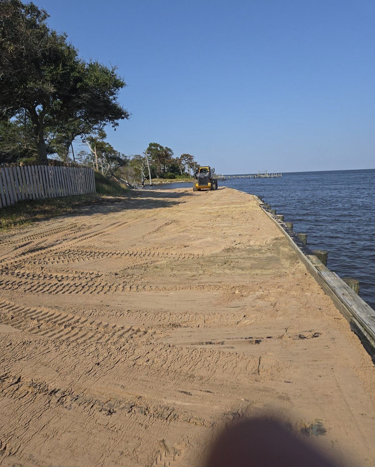 Sandy waterfront path with tire tracks, small machinery, and ocean on a sunny day.