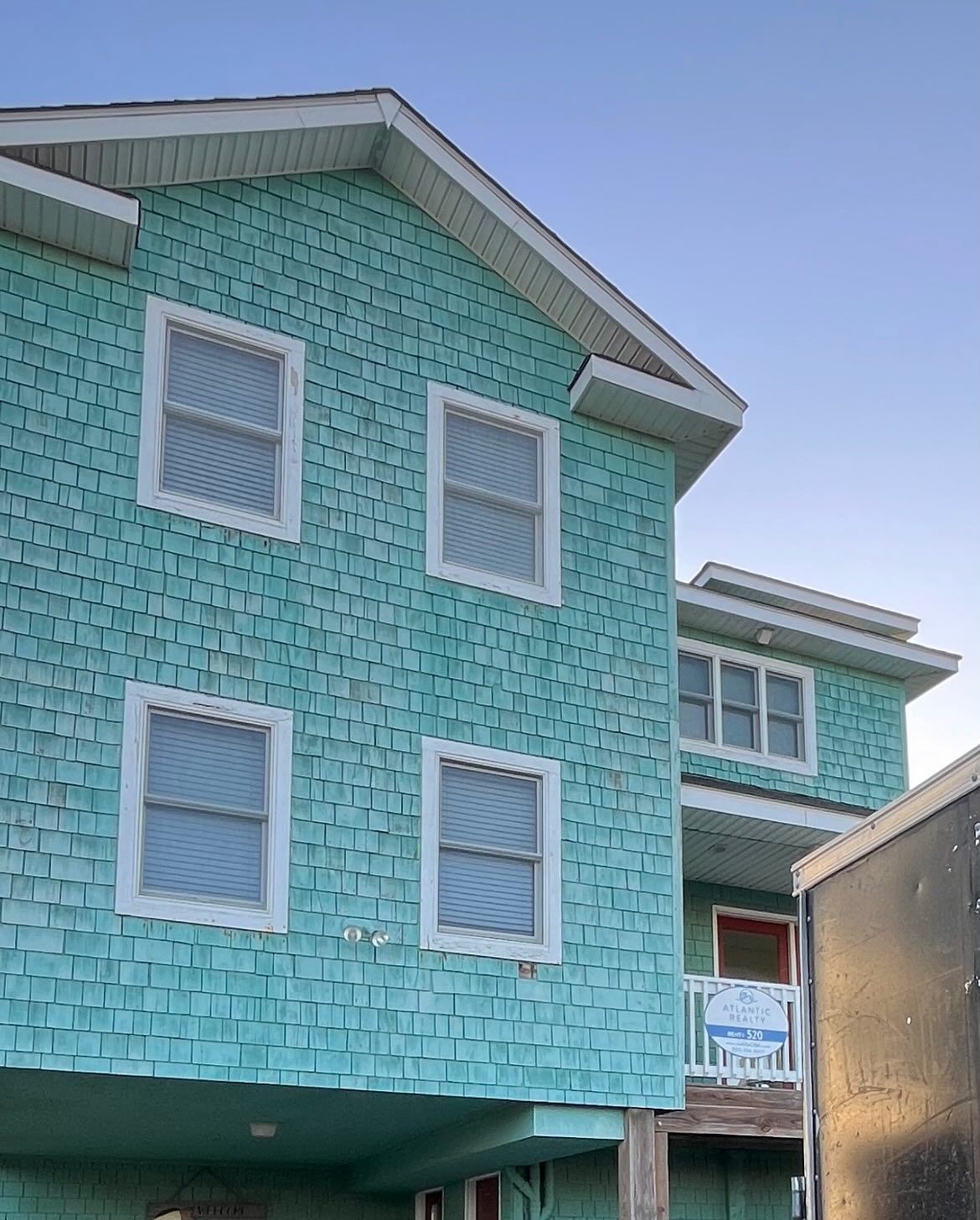 Two-story turquoise house with white-framed windows and shingle siding. A second similar building is partially visible.