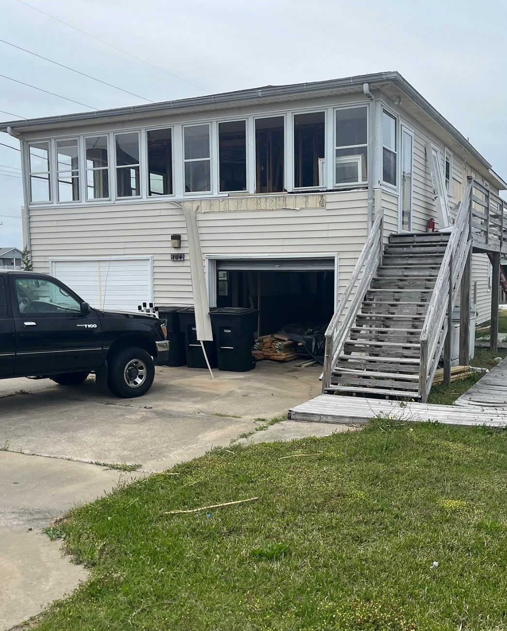 Two-story house with a garage, stairs, and black truck. Weathered exterior, cloudy day.