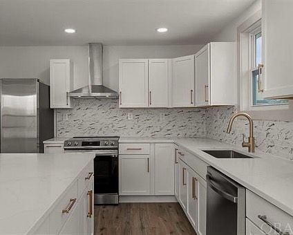 Modern white kitchen with stainless steel appliances, copper hardware, and a marbled backsplash.