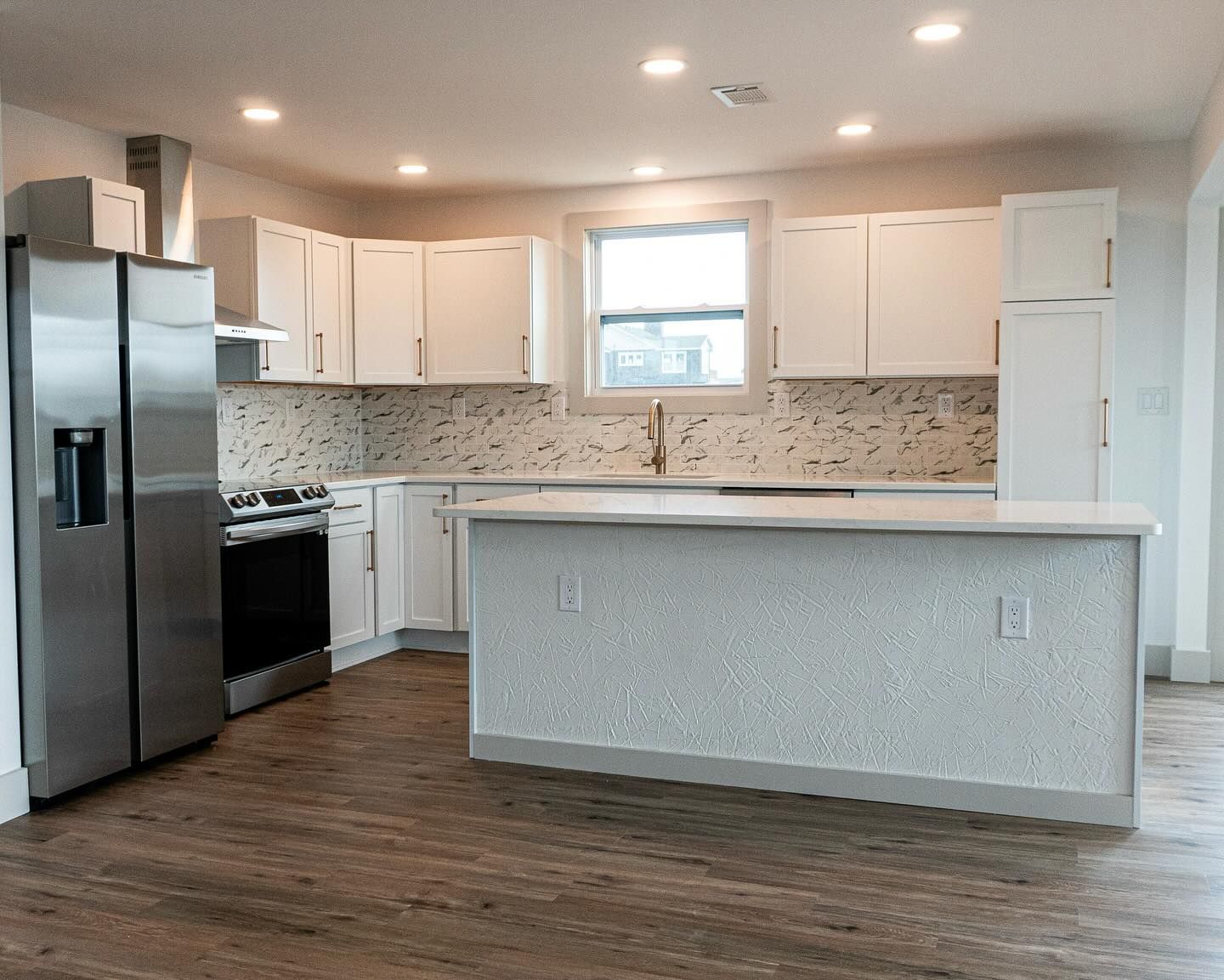 A bright, modern kitchen featuring white cabinets, a stainless steel refrigerator, and a large island with