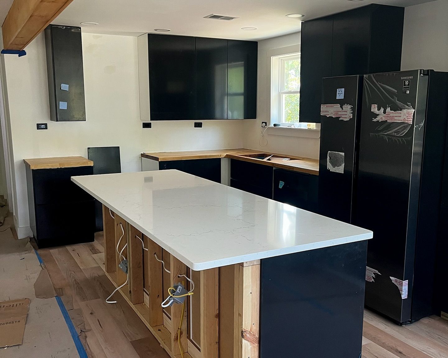 Kitchen under renovation with black cabinets, white countertops, a large island, and a mounted TV.
