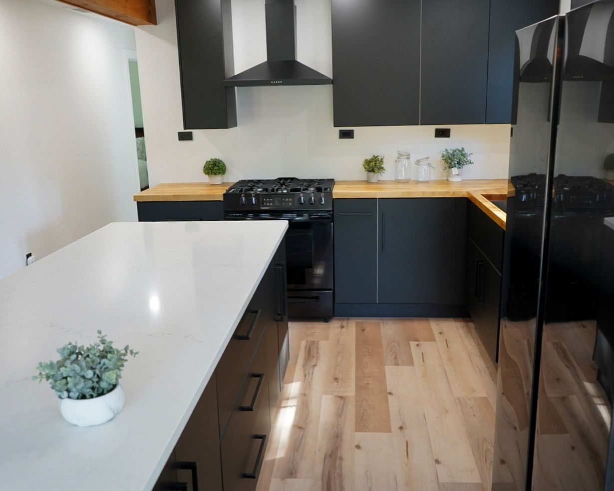 Modern kitchen with black cabinets, wooden countertops, and a white island. Black appliances and light wood floors.