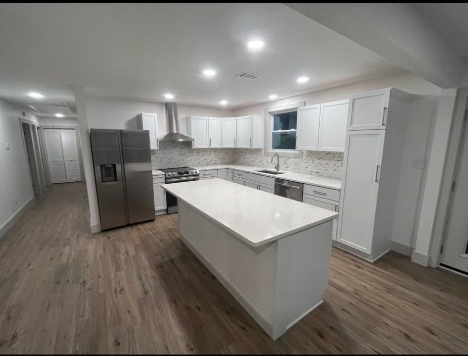 Newly renovated kitchen with white cabinets, stainless steel appliances, and an island. Light wood floorin
