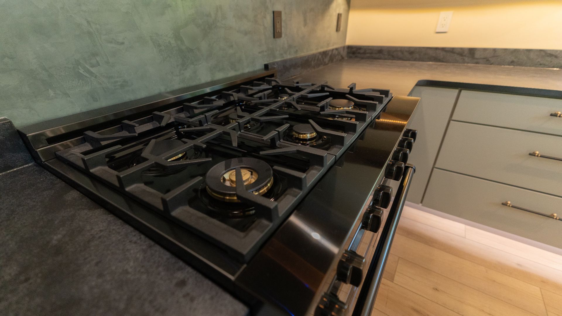 Black gas stovetop on a gray countertop. Light green cabinets are to the right.