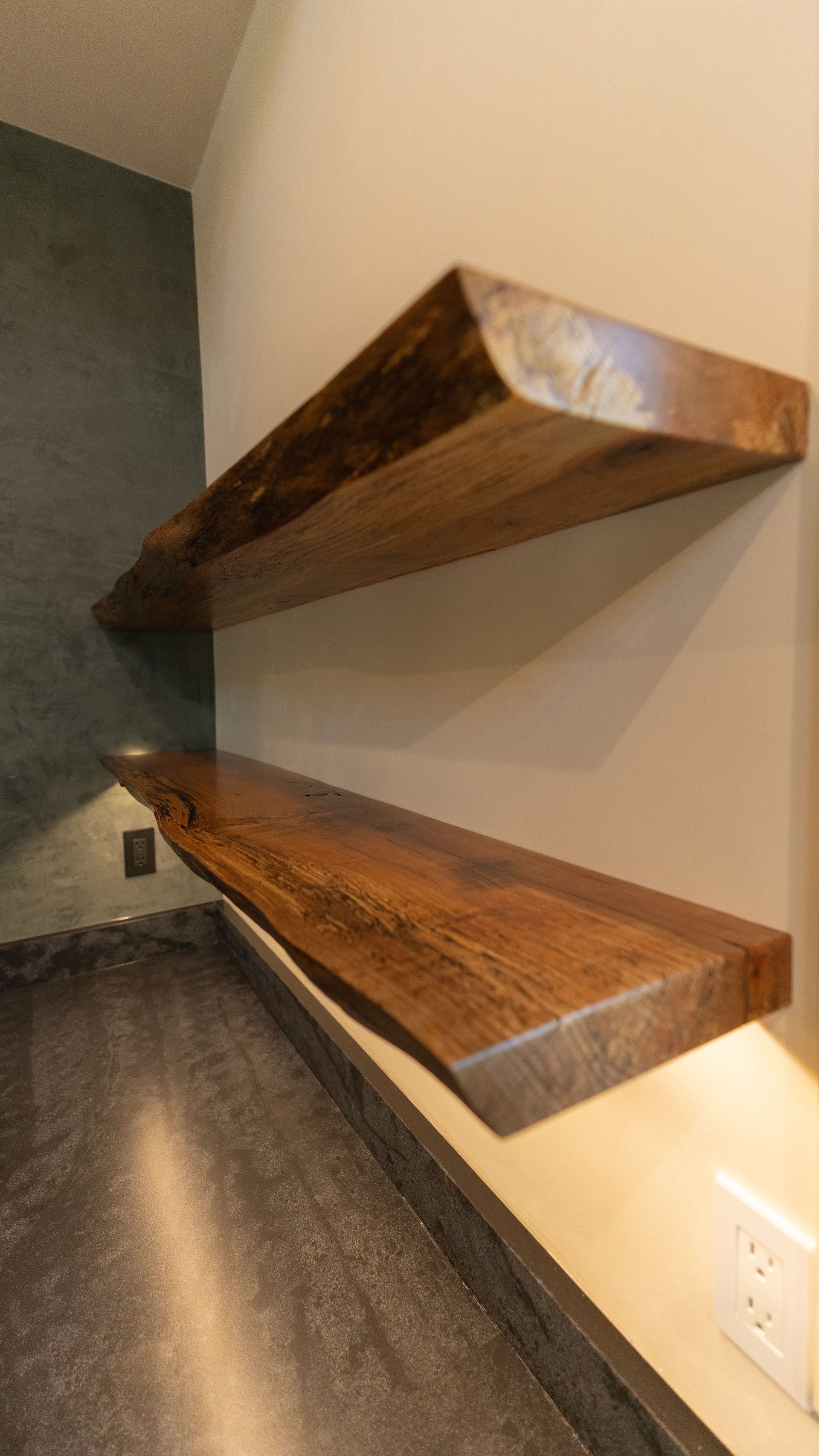 Two floating wooden shelves of varying lengths, mounted on a tan wall above a dark countertop.