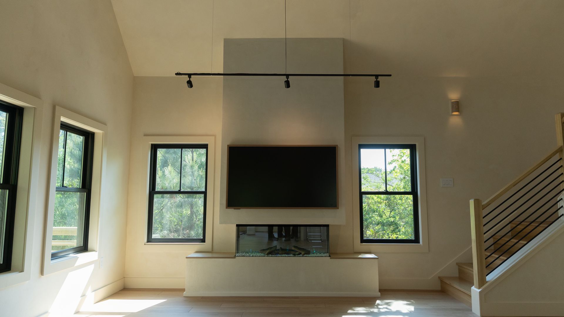 Living room with fireplace, TV, windows, and stairs. White walls, black trim.