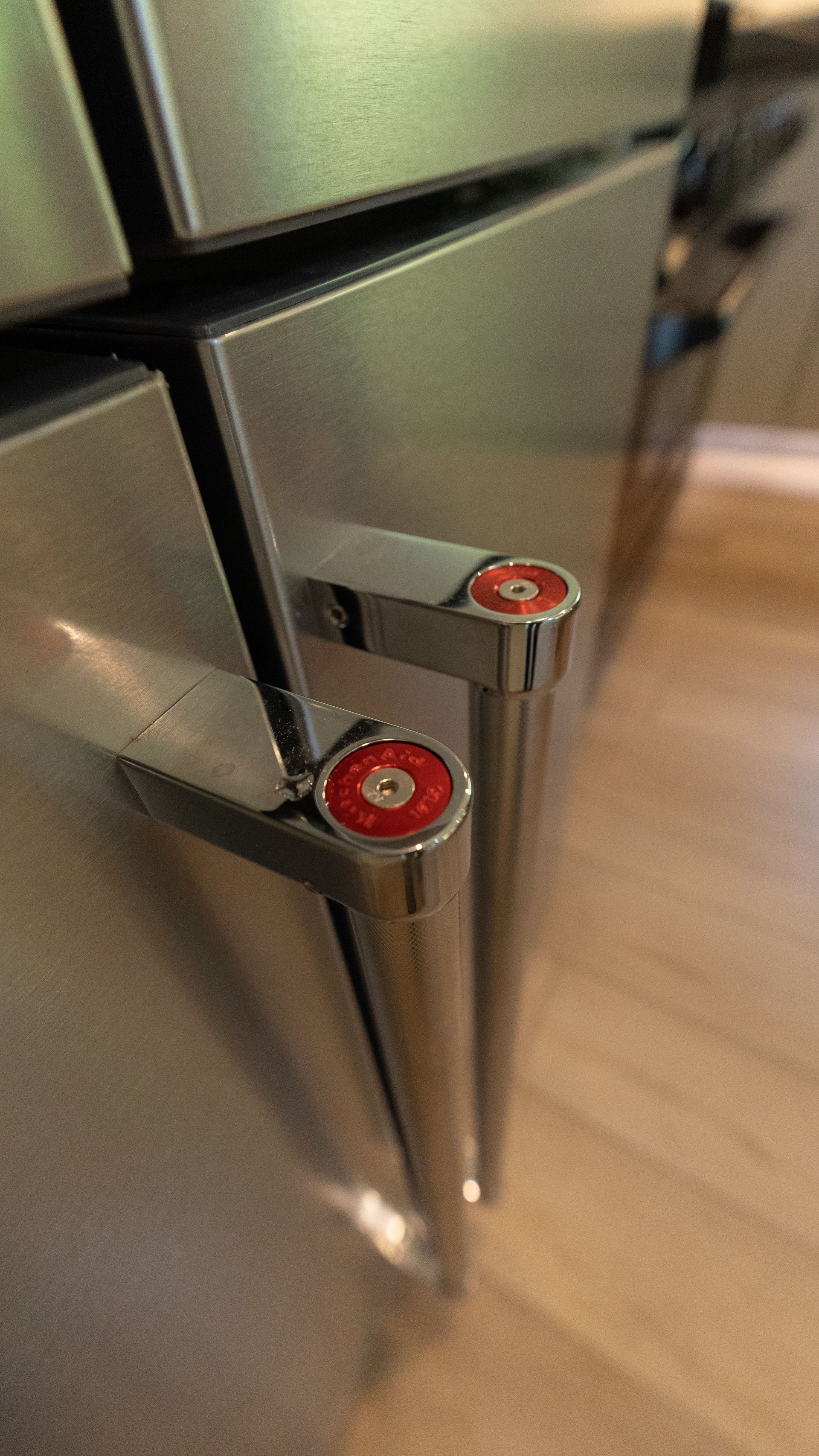 Stainless steel refrigerator doors with chrome handles, red accents, and wooden floor.
