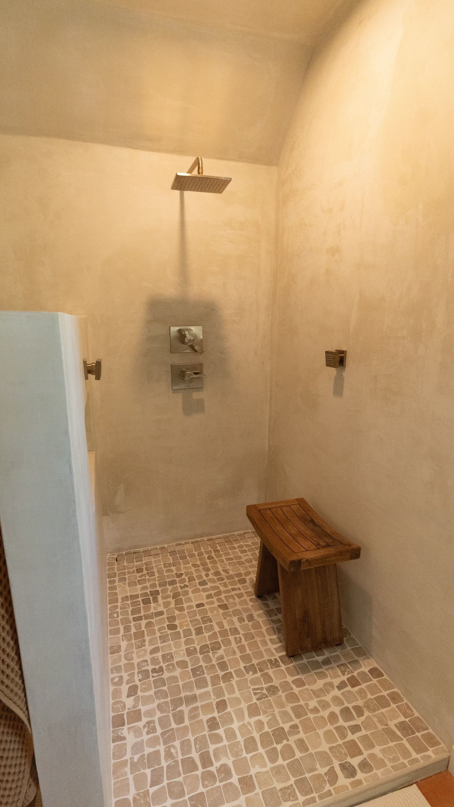 Shower with a stone bench, tiled floor, and wall-mounted shower head in a warm-toned space.
