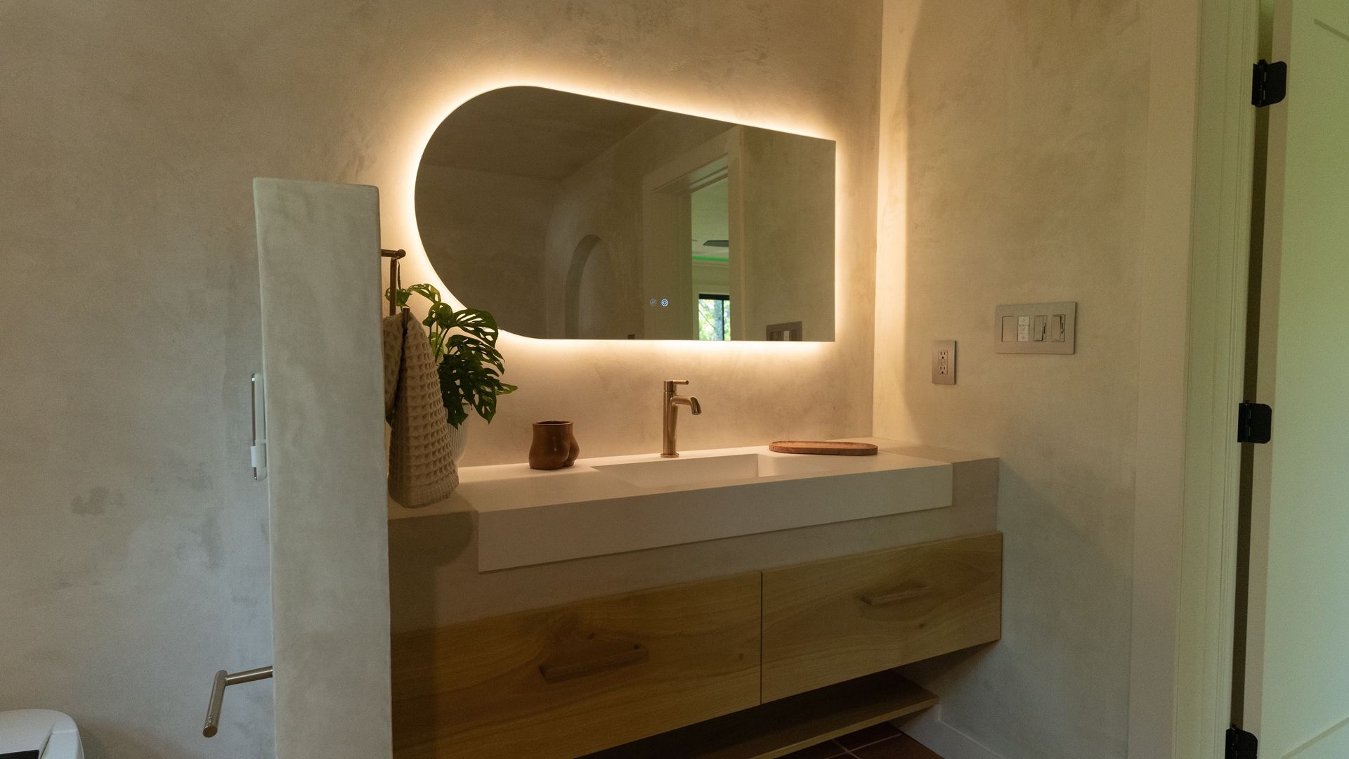 Modern bathroom with lit mirror, floating vanity with wooden drawers, and neutral-toned walls.