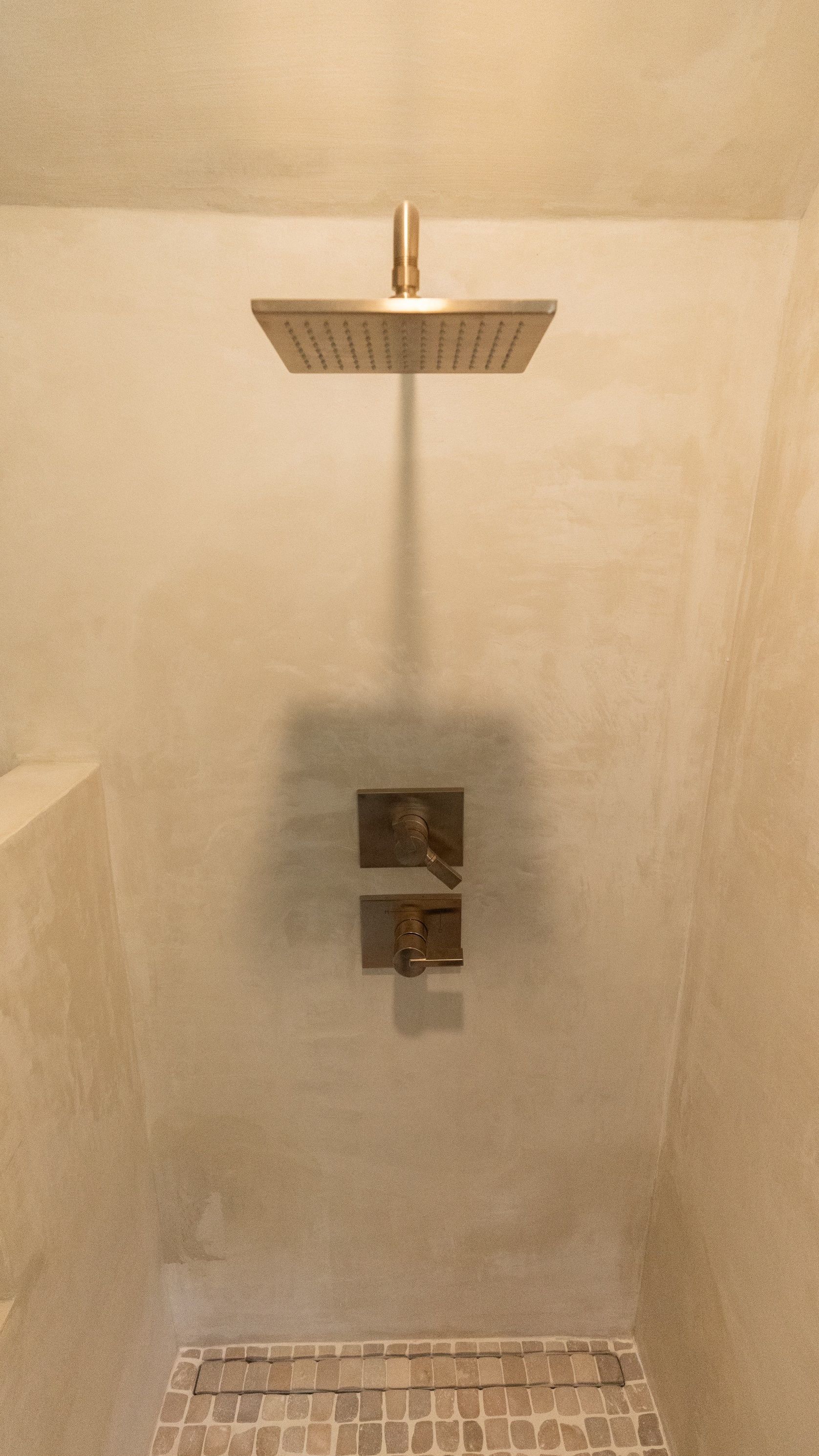 Modern shower with a square rain showerhead, bronze fixtures, and a mosaic tile base.
