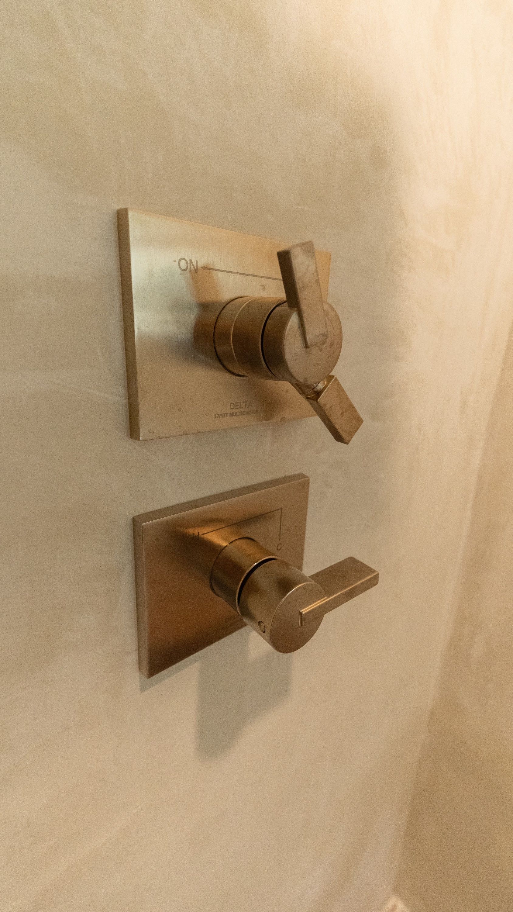 Brushed nickel shower faucet controls on a beige wall. Top is temperature, bottom is water flow.