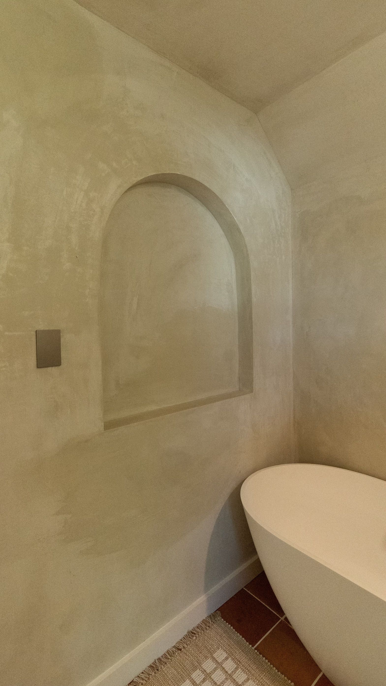 Bathroom corner with recessed arched shelf, bathtub, and textured walls in neutral tones.