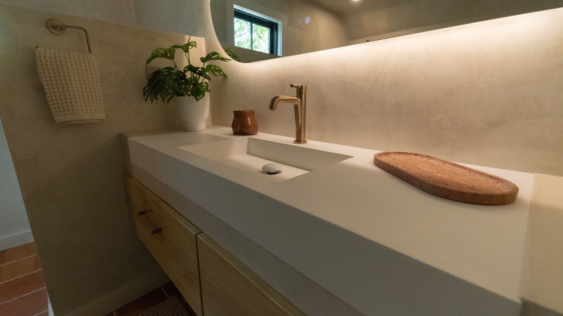 Bathroom with white counter, gold faucet, and wood accents.