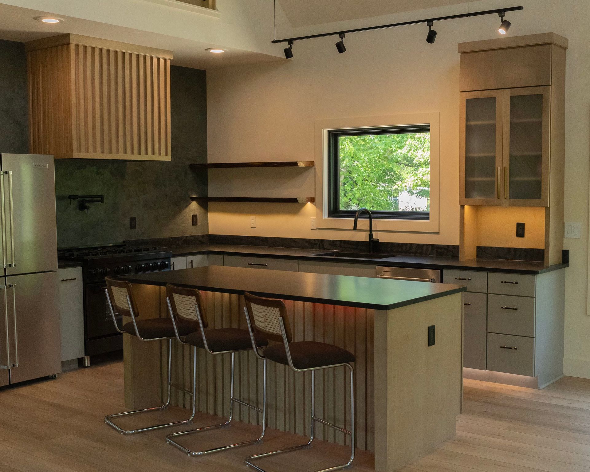 Modern kitchen with island and barstools, light cabinets, stainless steel appliances, and a window.