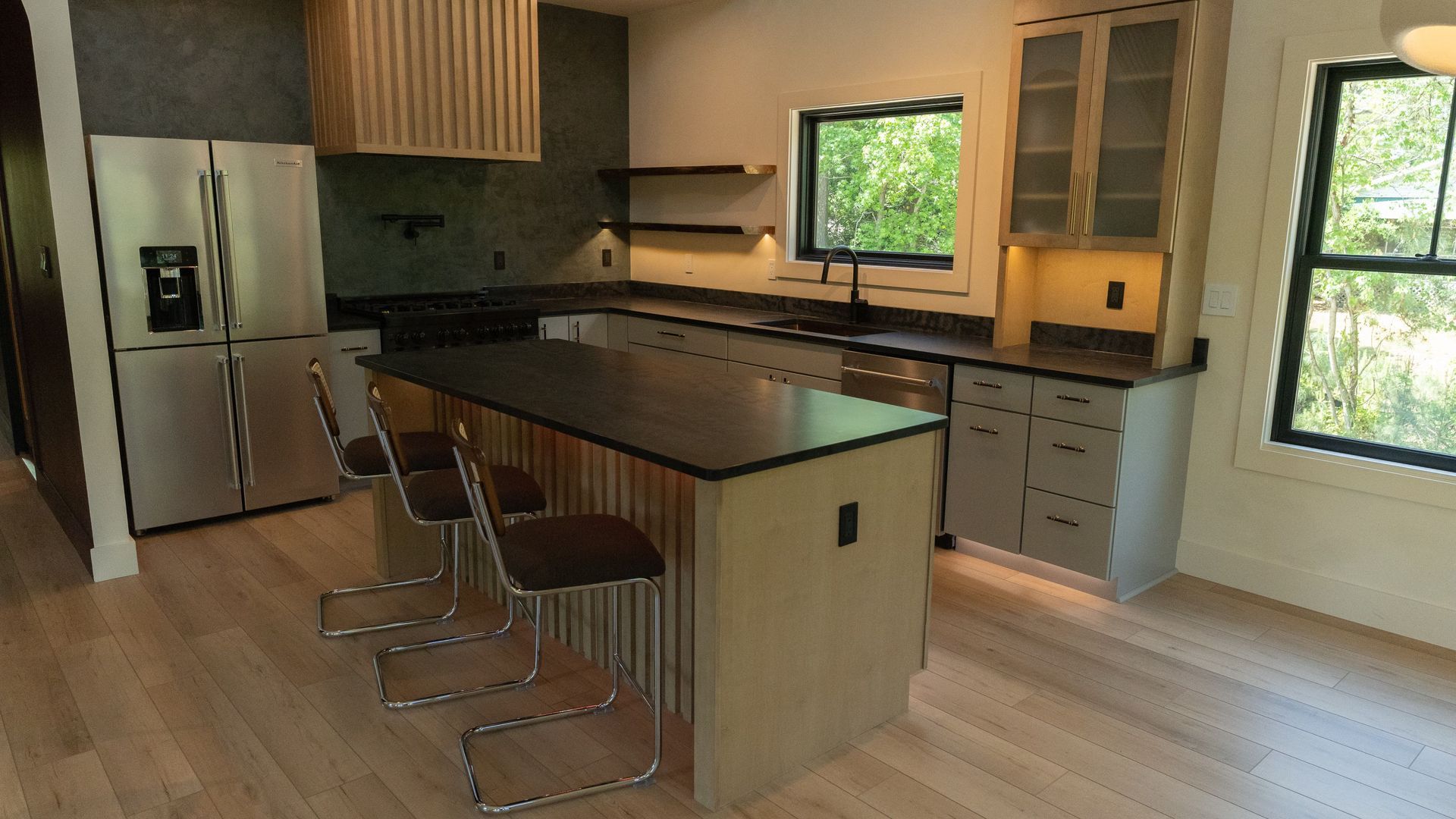 Modern kitchen with island, stainless steel appliances, gray cabinets, and wood floors.