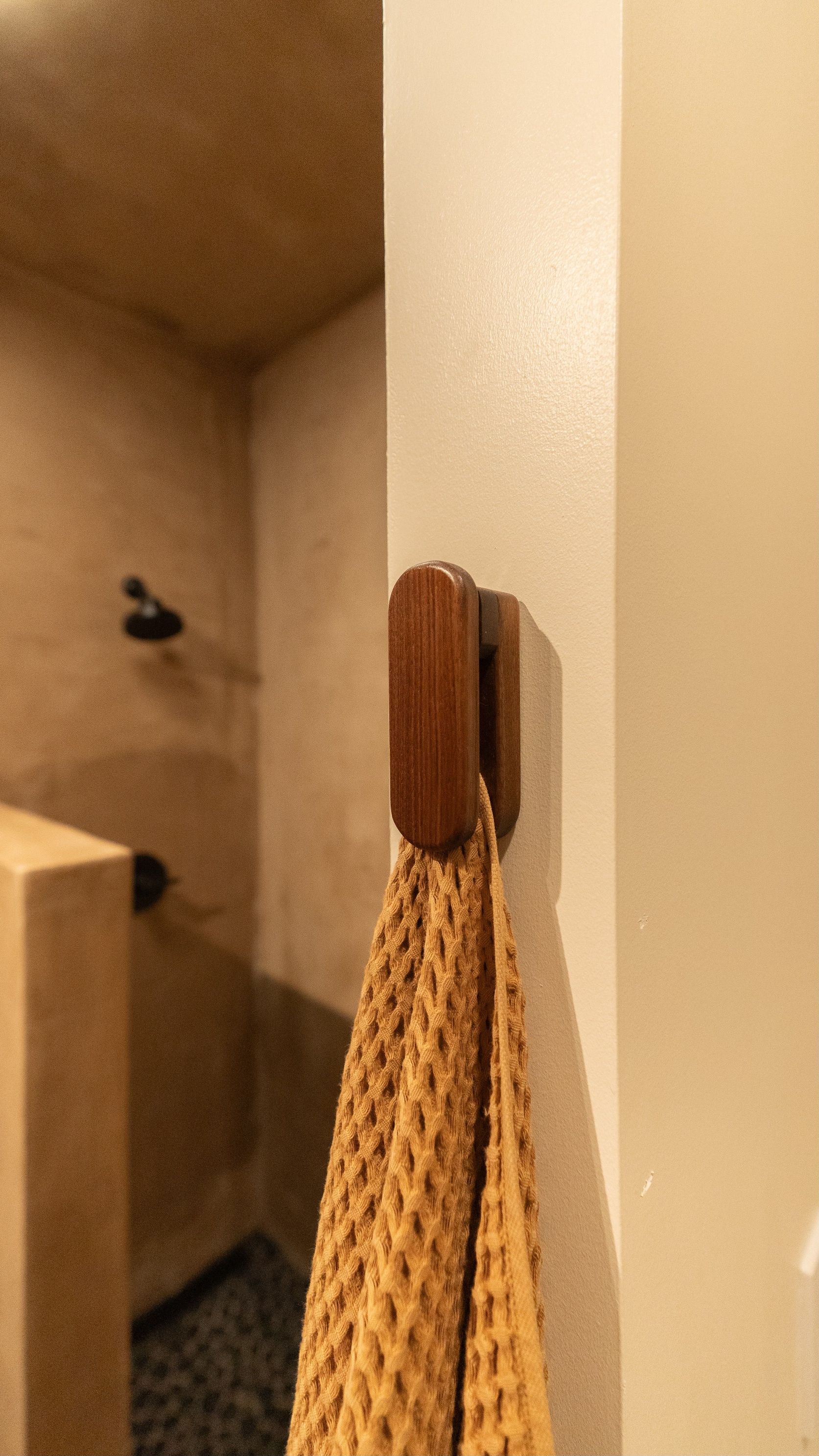 Towel hanging on a wooden hook on a beige wall near a shower.