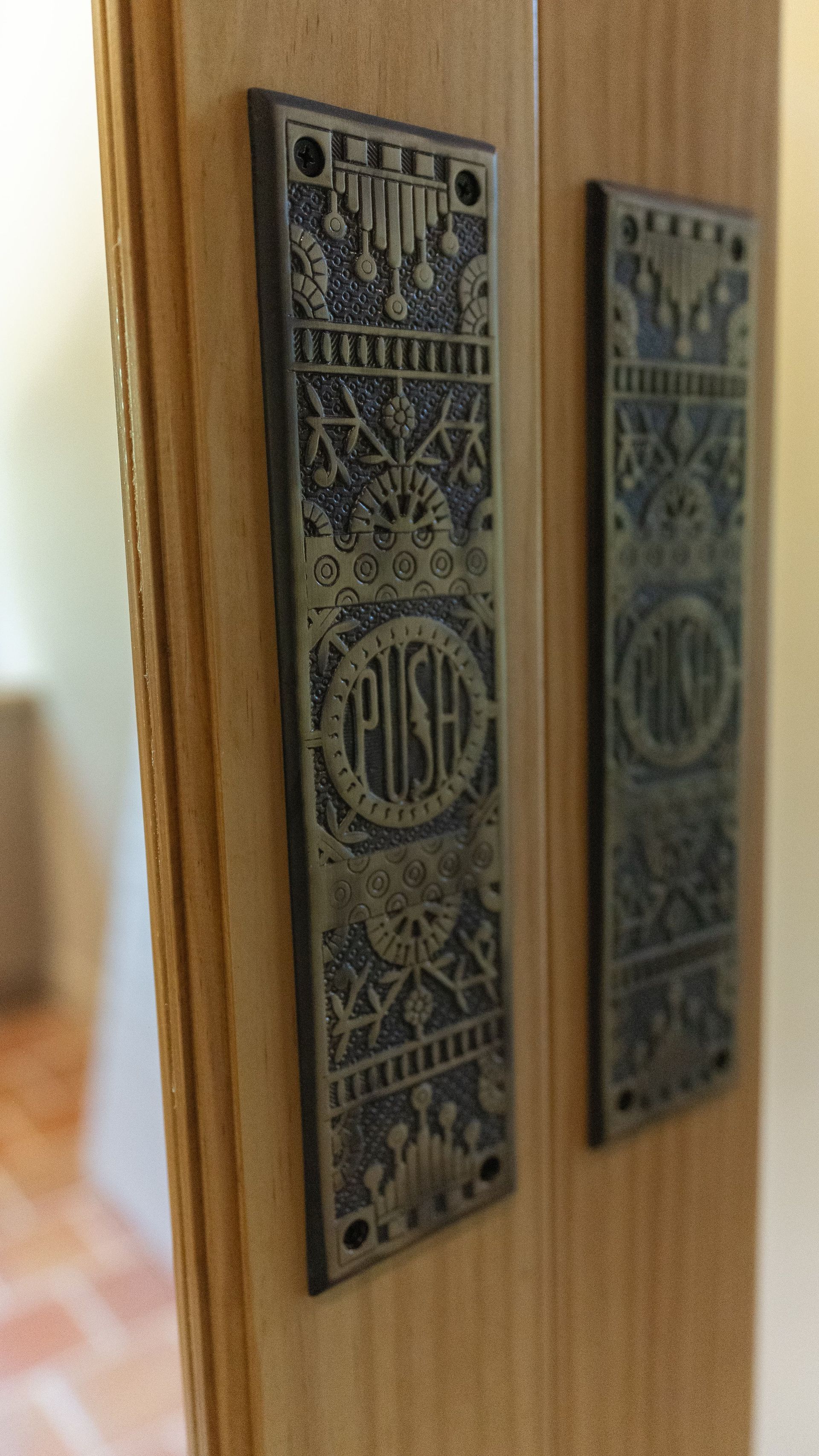 Two bronze push plates on a wooden door, each with 