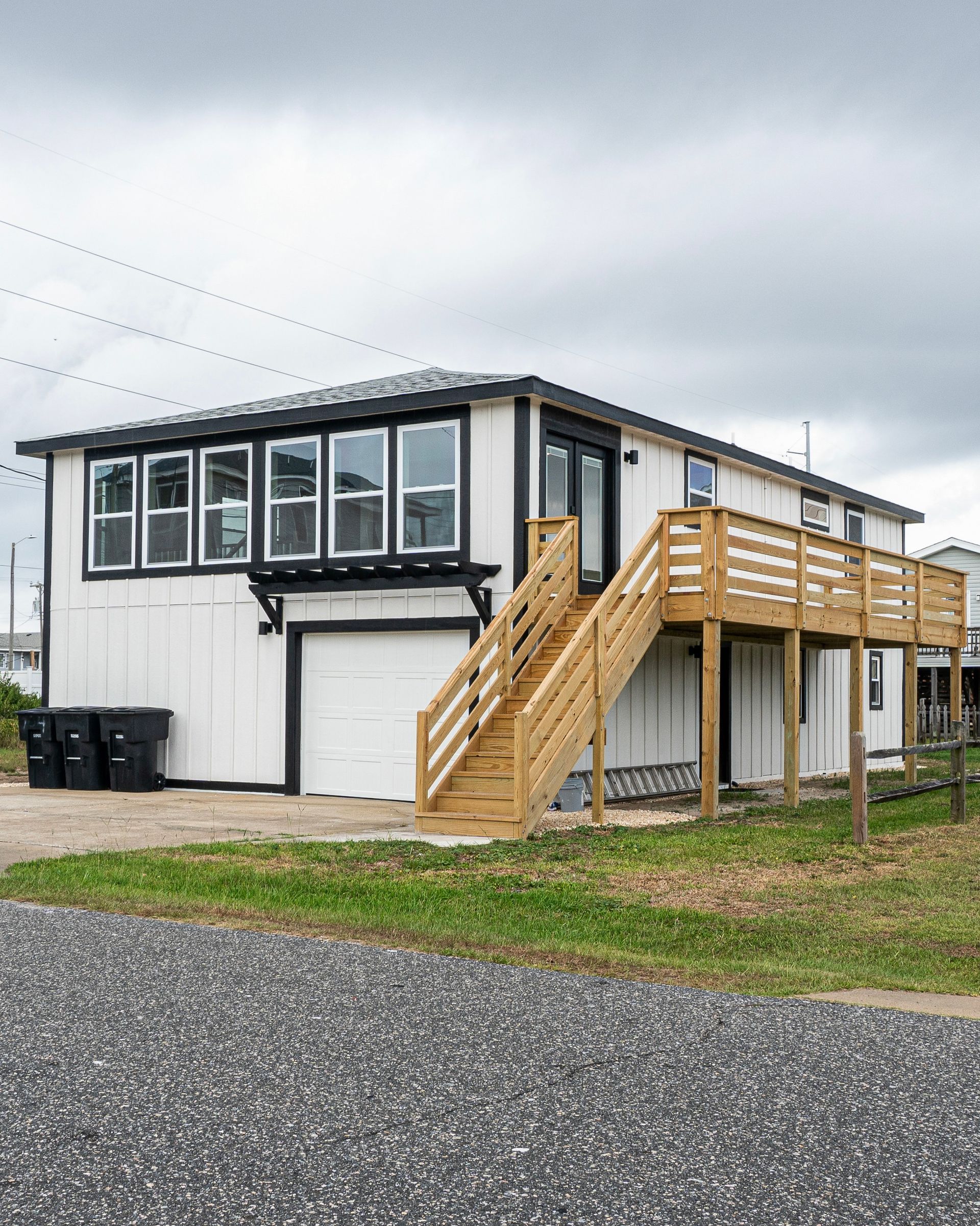 White house with black trim, wooden stairs leading to a deck, and a garage.
